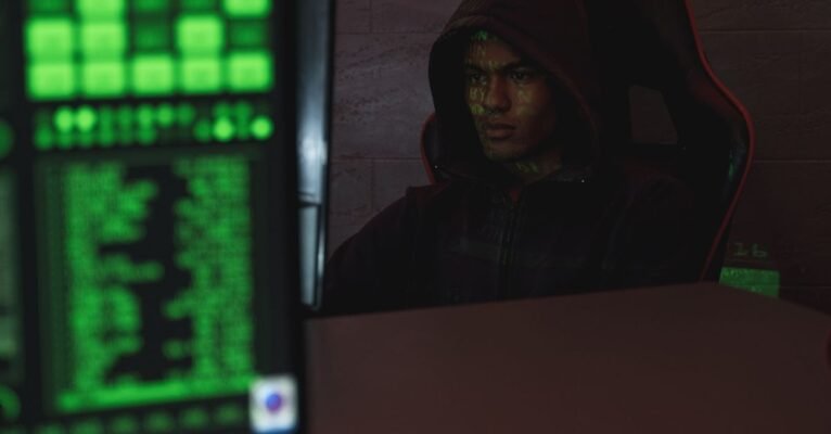 Hooded programmer intensely focused on computer screen, ensuring data protection and cyber security